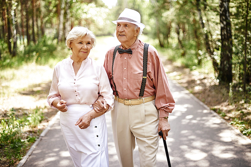 Elderly couple in smart casual-wear walking in summer park