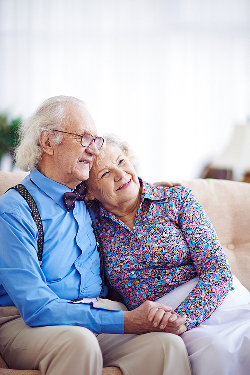 Affectionate aged couple in smart clothes having rest on sofa