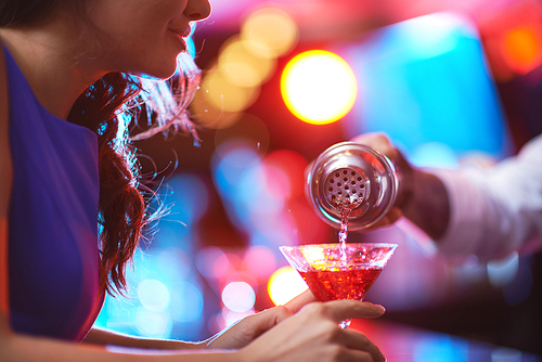 Girl holding martini glass while barman pouring cocktail