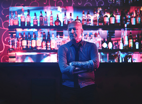 Mature bald man standing by bar counter in night clubv