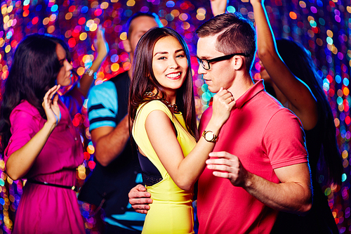 Amorous couple dancing at party with their friends on background