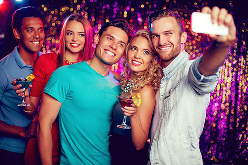 Company of cheerful friends making selfie at party