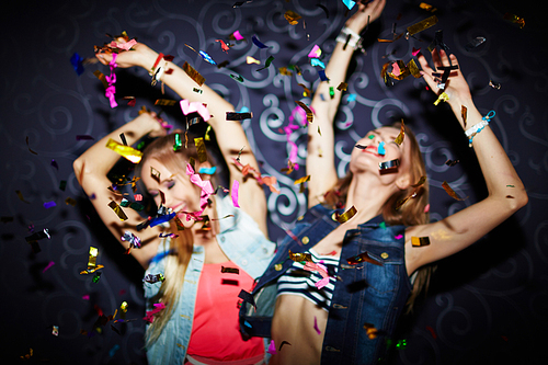 Two energetic girls dancing in confetti falling