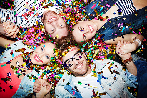 Cheerful friends lying on the floor covered with confetti in the night club