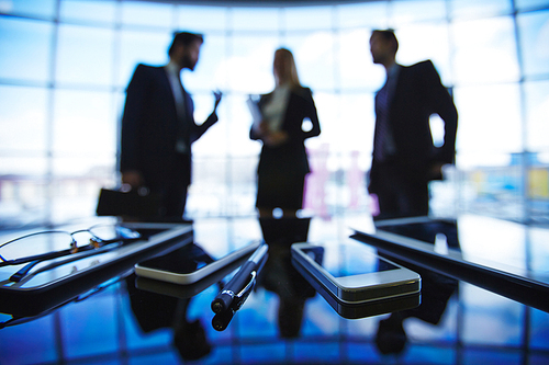 Modern gadgets with pen on background of business group talking