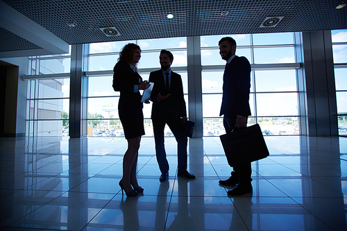 Silhouettes of three co-workers talking by the window