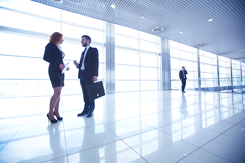 Two colleagues talking at business center with busy manager on background