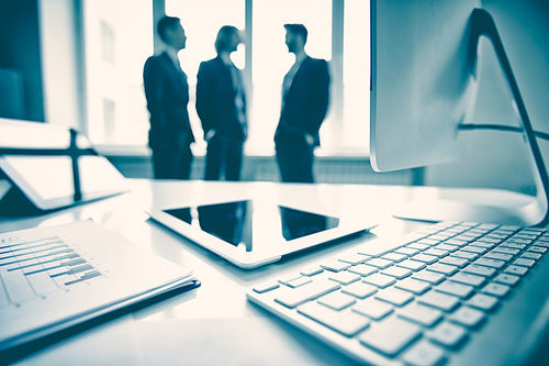 Touchpad, monitor, keypad and business document with group of businessmen on background