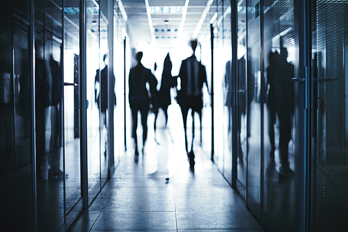 Blurred silhouettes of business people moving in aisle between offices