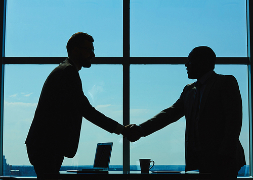 Outlines of two businessmen handshaking against window