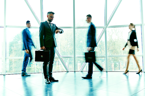 Elegant businessman waiting for partner on background of moving employees inside office building