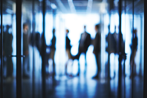 Blurred silhouettes of business people interacting in aisle of office center