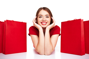 Smiling shopper lying between two red paperbags