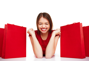 Joyful girl with expression of triumph lying between red paperbags