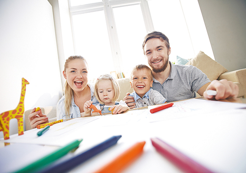 Happy young couple and their two adorable children drawing together