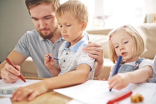 Young man teaching his son to draw with cute girl near by
