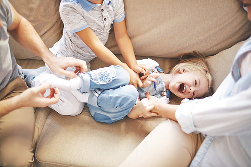 Happy girl laughing while her mother and brother tickling her
