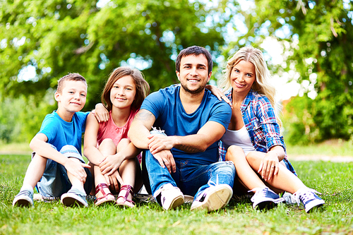 Happy young parents and their children relaxing on lawn