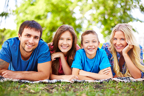 Happy family of four lying in park and enjoying summer rest