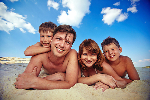 Young couple and two siblings lying on sand under cloudy sky