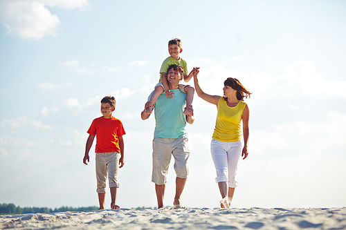 Happy family in casualwear walking on sandy beach
