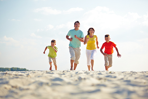 Modern family in casualwear running on sandy beach