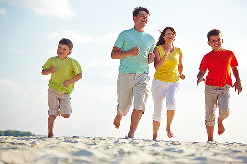 Modern family of four running on sandy beach