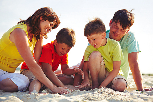 Young family in casualwear playing with sand on beach