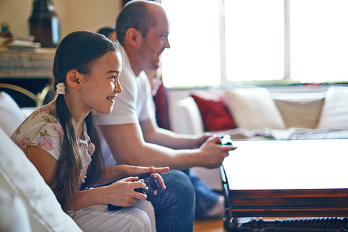 Smiling girl playing video games with her father