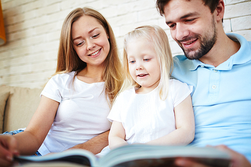 Happy young couple and their daughter reading at home