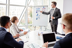 Elegant businessman by whiteboard explaining his viewpoint upon financial fluctuation to his employees