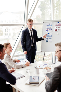 Young employee pointing at data on board and looking at his colleagues