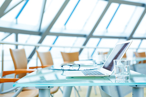 Laptop and glass of water on workplace in empty conference hall