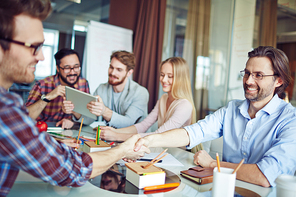 Businessmen handshaking on background of working team