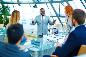 African-american businessman standing by whiteboard and voicing his opinion about data analysis to colleagues