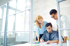 Young employer signing contract with his colleagues near by