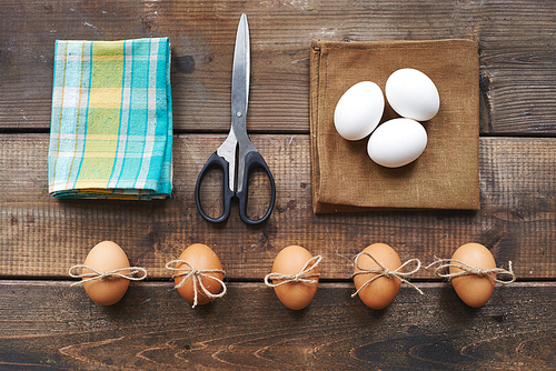 Different eggs, scissors, linen and cotton napkins on wooden background
