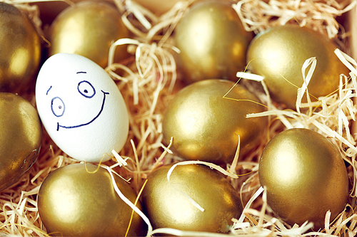 Egg with smiley face among golden eggs