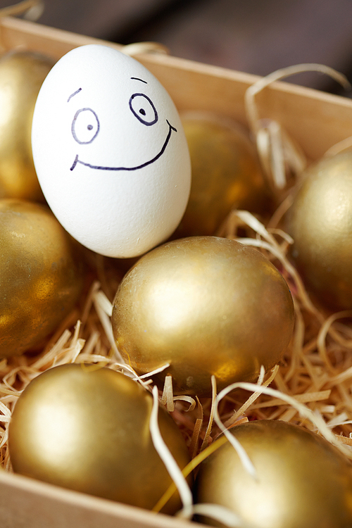 Egg with painted face smiling among golden ones