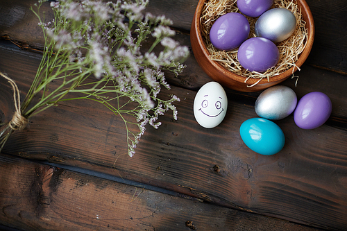 Colorful Easter eggs, smiling white egg and dry flowers near by