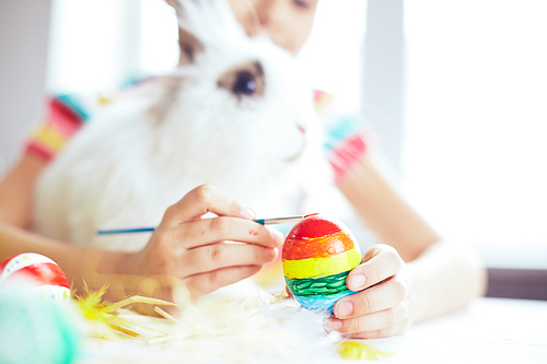 Girl painting an egg and embracing Easter rabbit