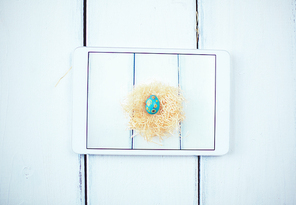 Touchpad on wooden background with Easter egg in nest