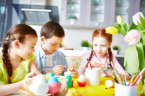Little friends painting Easter eggs in the kitchen