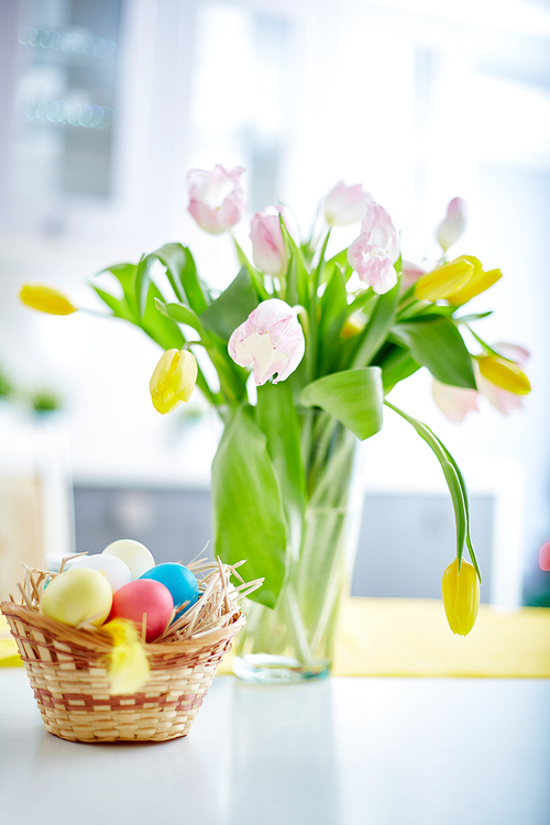 Easter eggs in basket and bunch of fresh tulips in vase