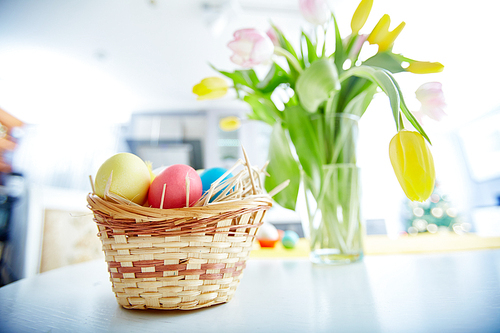 Easter eggs in basket with bunch of tulips on background
