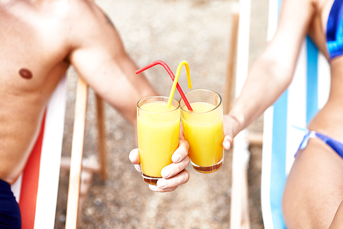 Glasses with fresh orange juice and straws held by couple