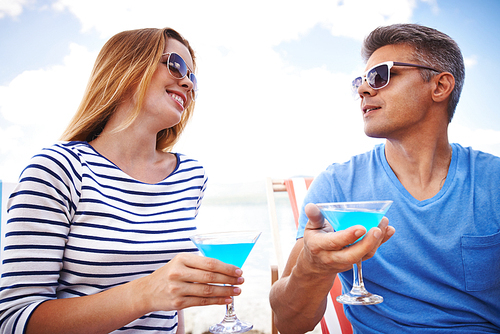 Young couple in eyeglasses toasting with martini during summer vacations