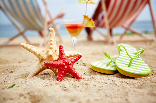 Two sea stars on sandy beach with cocktail and flipflops near by