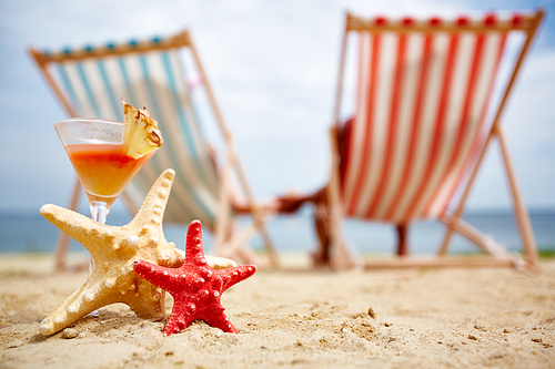 Two sea stars and tropical cocktail on sandy beach