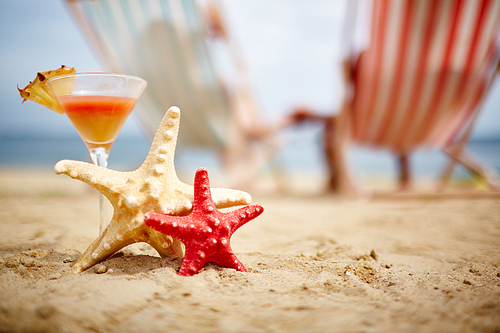 Two sea stars on sandy beach with tropical cocktail near by